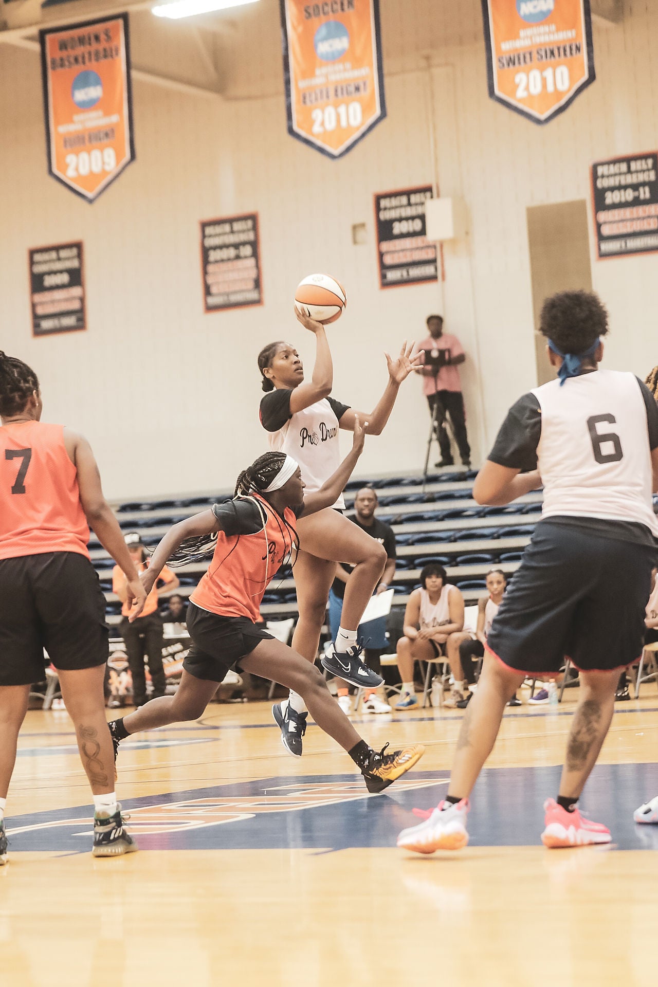 Basketball game in progress with players on a court, banners on the wall.